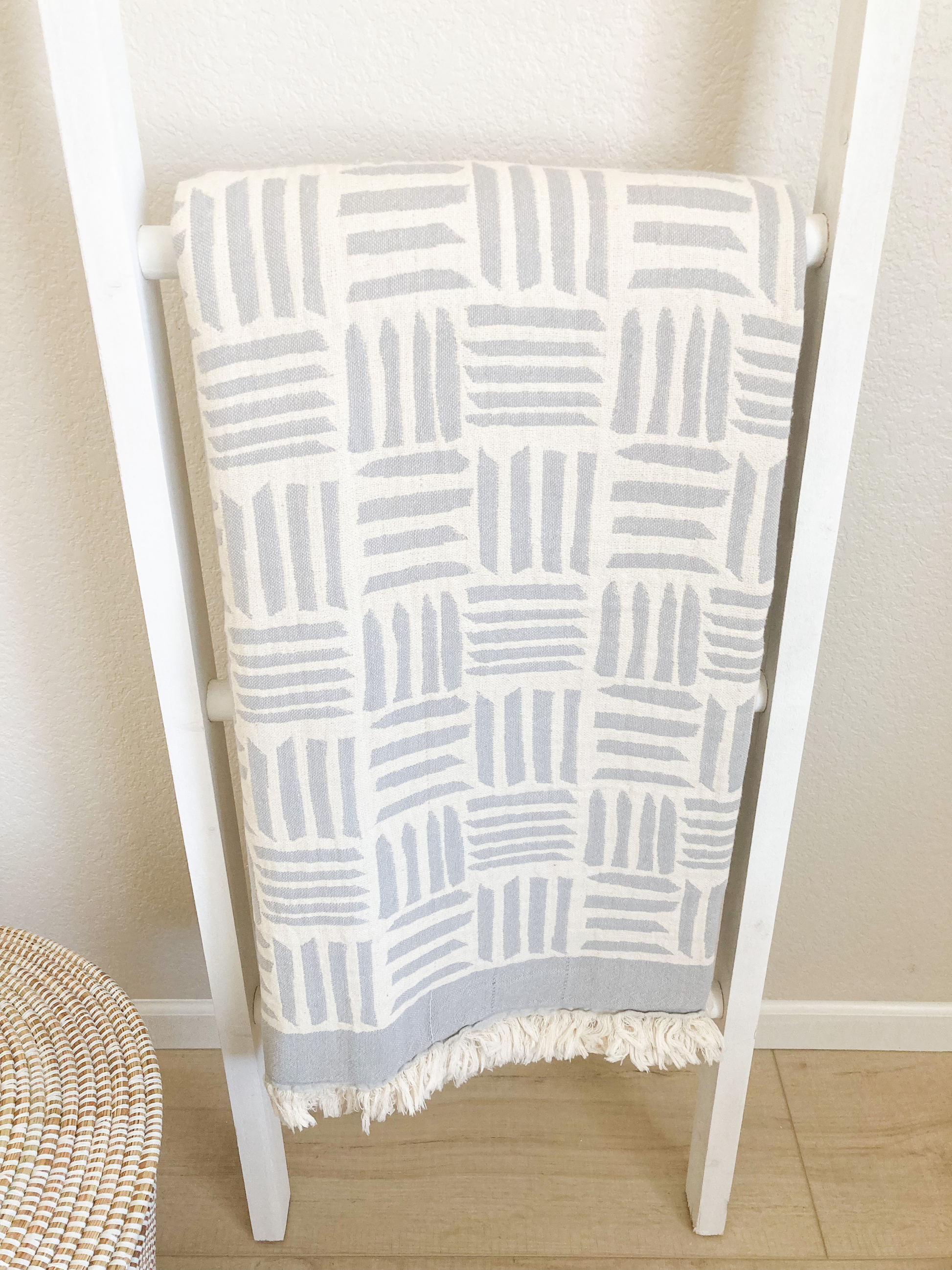 Light gray and ivory blanket hanging on a blanket ladder. The blanket has a modern geometric pattern. Close Up view of the blanket.